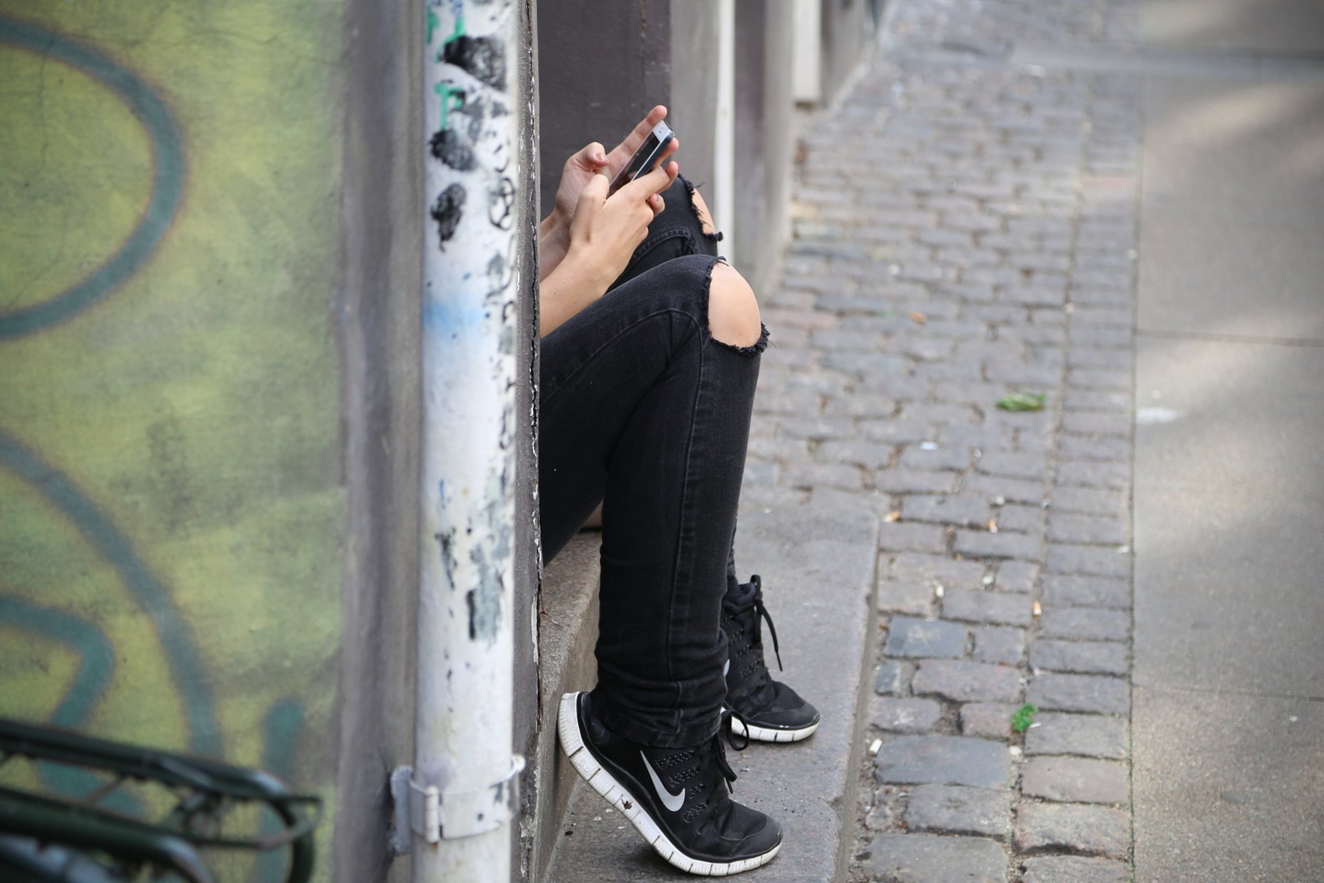 Junger Mensch sitzt in einem Türeingang und schaut ins Smartphone.
